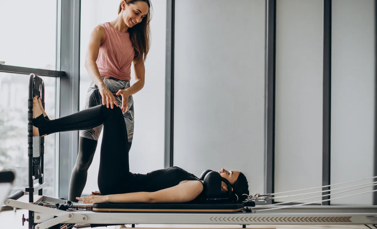 Instructora guiando a una alumna en una clase de iniciación de Pilates Reformer