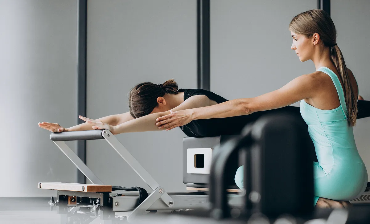 Instructora asistiendo a una alumna durante un ejercicio de Pilates Reformer Terapéutico