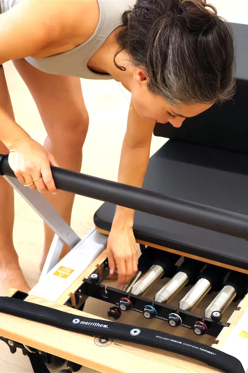 01-pilates10-les-corts-barcelona Instructora ajustando una máquina de Pilates Reformer en Pilates10 Les Corts